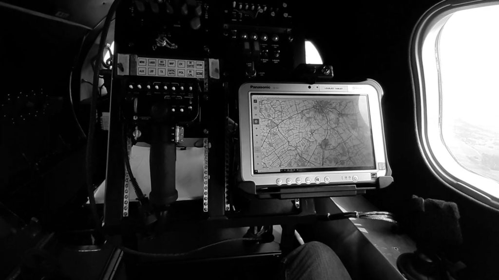 Black and white Interior of a jet; Looking at a computer with a map and controls. Window to the right of the computer. 