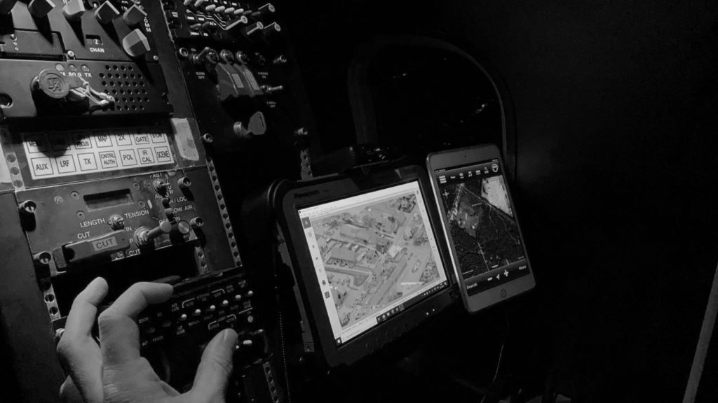 Black and white image of the left hand of an operator adjusting controls on the control panel next to two screens.