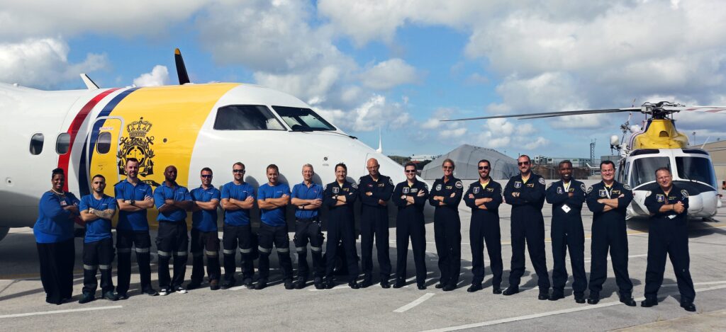 DCCG and PAL Aerospace crew standing abreast, arms crossed in front of fixed and rotary wing DCCG aircraft