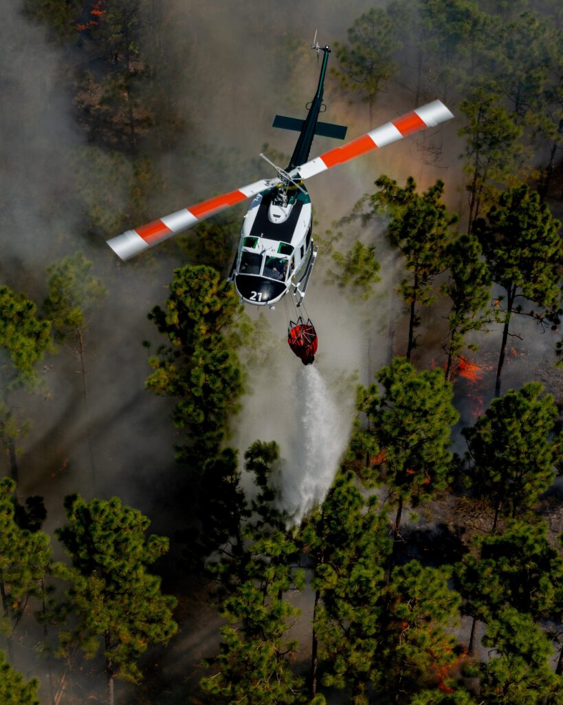 A firefighting helicopter releases a bucket load of water over burning timber.