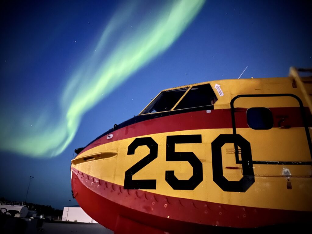 The nose of water bomber 250 on the ramp at night, with the aurora overhead.