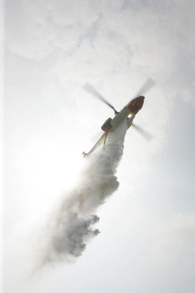 A firefighting helicopter releases its load while almost entirely obscured by smoke and cloud.