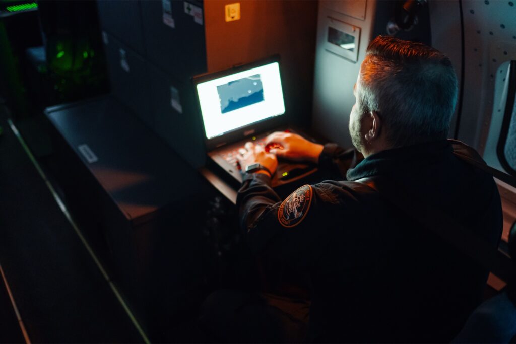 A sensor operator works a mission display in a darkened aircraft cabin during a night sortie.